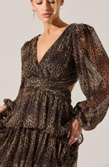 A woman is wearing a dress with a leopard print pattern. The dress features a V-neckline, puffed long sheer sleeves with elastic cuffs, a fitted waist with a wide waistband, and a tiered, ruffled skirt. The fabric appears lightweight and semi-transparent.