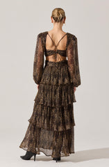 A woman is wearing a long, tiered skirt and a matching crop top with long, sheer, puffed sleeves featuring a leopard print pattern. The top has thin, criss-crossing straps at the back and ties in the center. The skirt has multiple ruffled layers with the same leopard print pattern. She is also wearing black high-heeled boots.