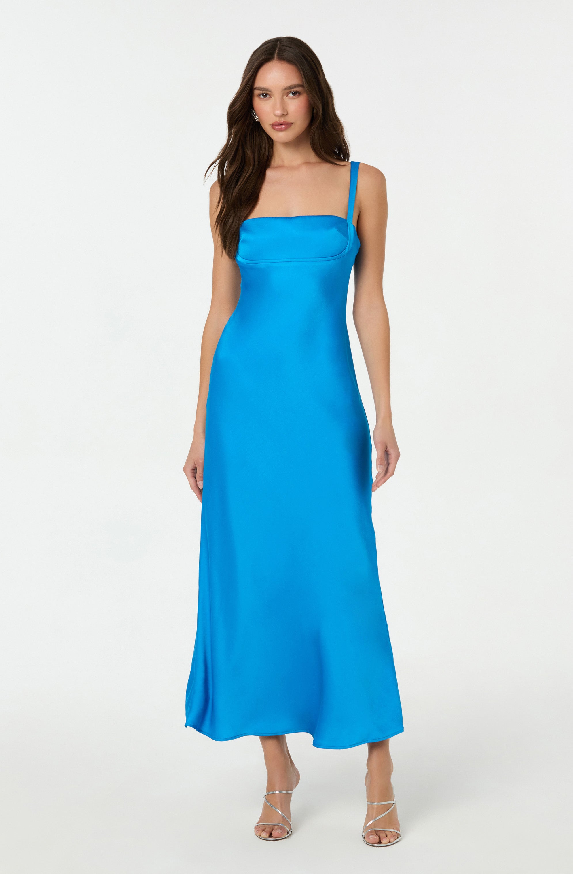 The woman is wearing a long, bright blue satin dress with a straight neckline and thin shoulder straps. She is also wearing strappy high-heeled sandals.