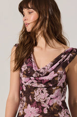 A woman is wearing a sleeveless dress with a cowl neckline and a floral pattern featuring shades of pink, purple, and brown.