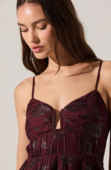 A woman wearing a deep burgundy dress with thin spaghetti straps. The dress features a textured pattern with black and metallic accents, and has a small keyhole opening at the chest.