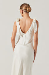 A woman wearing a sleeveless, cream-colored satin dress with a deep V back and shoulder ties. The fabric appears smooth and shiny, giving an elegant and sophisticated look.