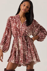 A woman is wearing a long-sleeved dress with a V-neck and a drawstring waist. The dress features an animal print pattern in shades of brown and cream, with a loose, flowing skirt.