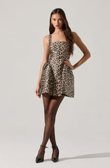A woman is wearing a sleeveless, fitted dress with a leopard print pattern that features a square neckline and thick straps. She pairs the dress with sheer black stockings and black high-heeled shoes.