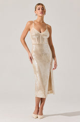 A woman is wearing a sleeveless, full-length dress made of shiny, cream-colored, sequin fabric. The dress features thin spaghetti straps, fitted bodice with a subtle curve at the bust, and a high slit at the front. She is also wearing cream-colored high heels.