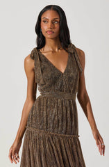 A woman is wearing a sleeveless dress made of shimmery, metallic fabric in shades of brown, gold, and bronze. The dress features shoulder straps tied into bows. It has a V-neckline, a fitted waist, and a gathered skirt with horizontal seams creating a tiered effect.