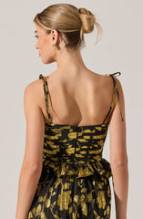 A woman is wearing a black dress with gold metallic patterns. The dress has thin shoulder straps tied into bows. The fabric features a shiny gold floral design on the skirt and a gold streaked pattern on the bodice.