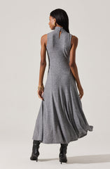 A woman is wearing a sleeveless, high-neck, grey dress that is fitted at the waist and flares out into a full, flowing skirt. She is also wearing black high-heeled boots.