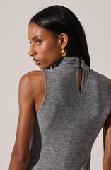 A woman is wearing a sleeveless, high-neck, grey textured top with a keyhole opening at the back, secured with a small button. She is accessorized with large, gold, teardrop-shaped earrings.
