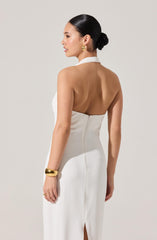 A woman is wearing a white, sleeveless evening gown with a halter neckline that ties at the back of the neck. The dress has a back zipper closure and a slit at the bottom. She accessorizes with gold hoop earrings, a wide gold bracelet on her right wrist, and a gold ring on her right hand.