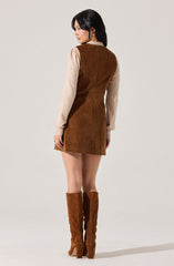 A woman is wearing a sleeveless brown suede dress with a straight cut, layered over a beige long-sleeve sweater. She also has on tall, matching brown suede knee-high boots with chunky heels. The outfit appears stylish and coordinated in earthy tones.