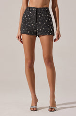 A person is wearing high-waisted black shorts with a textured fabric and a star pattern, paired with open-toe heels that have a sparkly, glittery design.