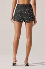 A pair of high-waisted black shorts decorated with white star and circle patterns, made from a textured fabric that appears to include sequins or embellishments. The shorts have a loose fit with a slightly curved hem. The model is also wearing high heels with metallic embellishments.