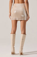 A person is wearing a high-waisted, short skirt covered in beige sequins, which creates a shiny, reflective surface. The skirt is paired with knee-high, light beige leather boots with pointed toes and stiletto heels. The outfit emphasizes a sleek and fashionable style.