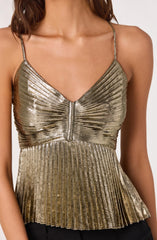 A woman is wearing a shiny, metallic gold sleeveless top with thin spaghetti straps. The top features a V-neckline and has horizontal and vertical pleats throughout, creating a textured, reflective surface. The fabric appears to have a slightly distressed or marbled finish, adding depth to the metallic look.