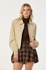 A woman wearing a beige zip-up jacket with elastic cuffs, a dark brown turtleneck sweater, and a high-waisted brown plaid skirt with a puffed, bubble style.