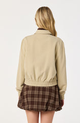 A person is wearing a beige, slightly oversized jacket with an elastic waistband and cuffs, and a folded collar. They are also wearing a brown checkered skirt with a loose, bubble-like fit.