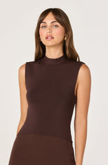 A woman is wearing a sleeveless, high-neck top in a dark brown color. The top has a fitted silhouette and appears to be made of a smooth, slightly textured fabric. She is also wearing gold earrings and has long, wavy brown hair.