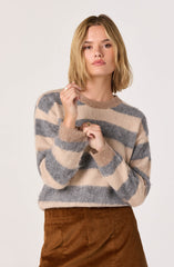 A woman is wearing a cozy, long-sleeved sweater with wide horizontal stripes in beige, gray, and taupe. The sweater has a soft, fuzzy texture and a round neckline. She is also wearing a high-waisted brown corduroy skirt.