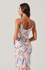A woman is wearing a sleeveless dress with thin shoulder straps. The dress features a colorful, graffiti-style print with words and phrases in red, blue, and light pink, covering the entire fabric.