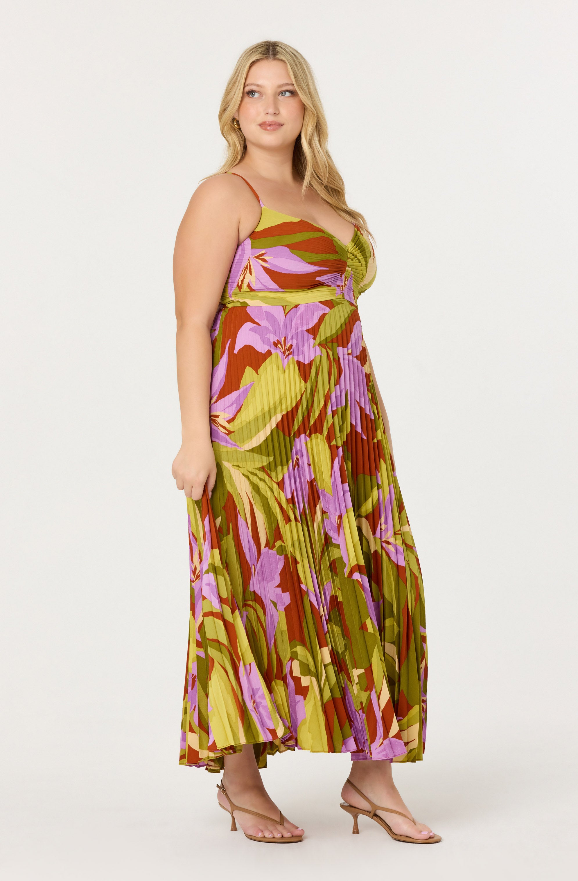 The dress features a colorful floral pattern with large, abstract flowers in shades of purple, pink, yellow, and green. It has thin spaghetti straps, a fitted bodice, and a flowing, pleated maxi skirt.