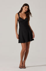 A woman is wearing a black sleeveless dress with lace trim along the neckline and shoulder straps. The dress has a fitted bodice and a flared skirt that falls above the knees. She has on black strappy high-heeled sandals.