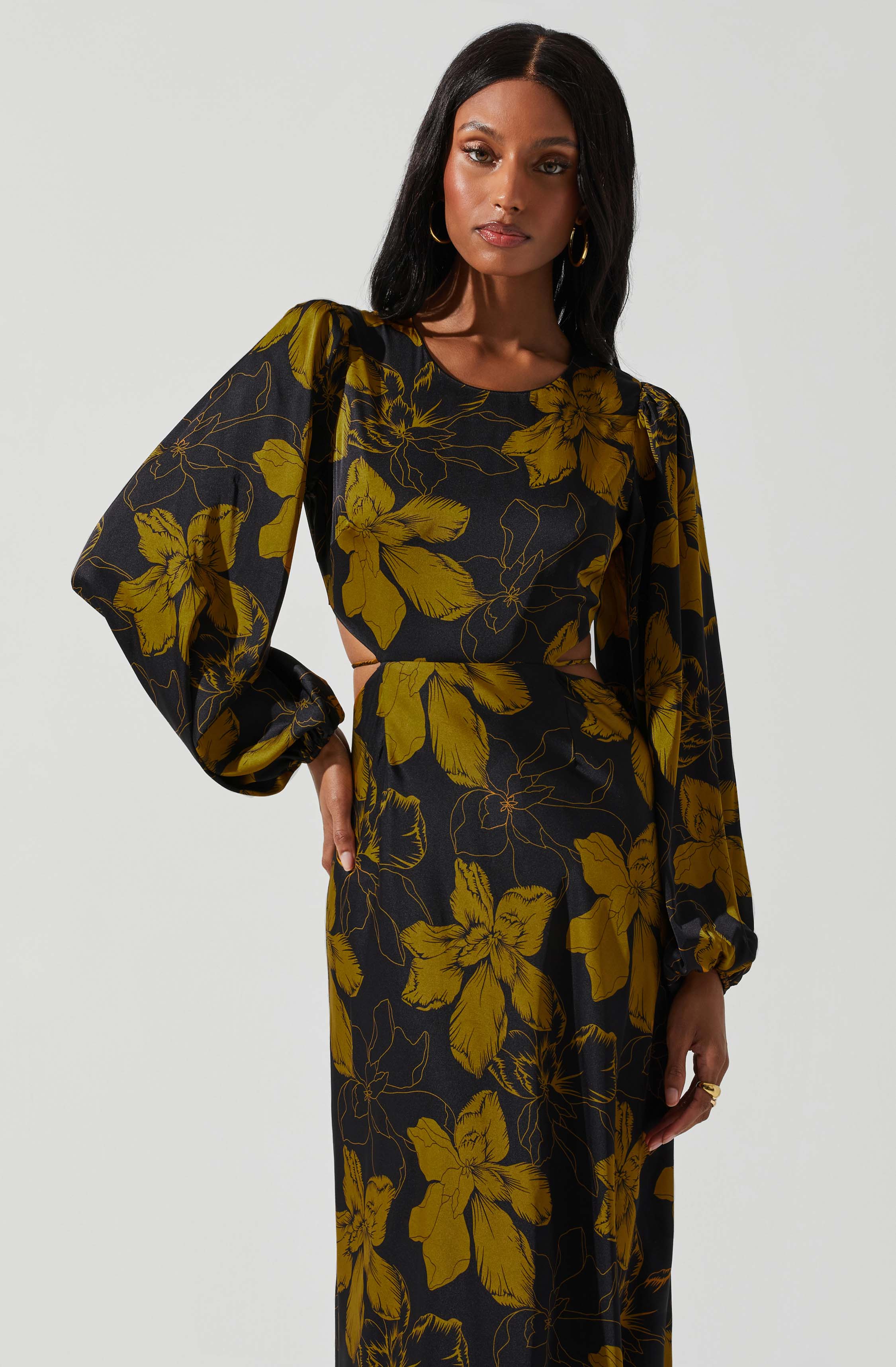 A woman wearing a black dress with large yellow floral patterns. The dress features long, voluminous sleeves with gathered cuffs and a fitted waist.