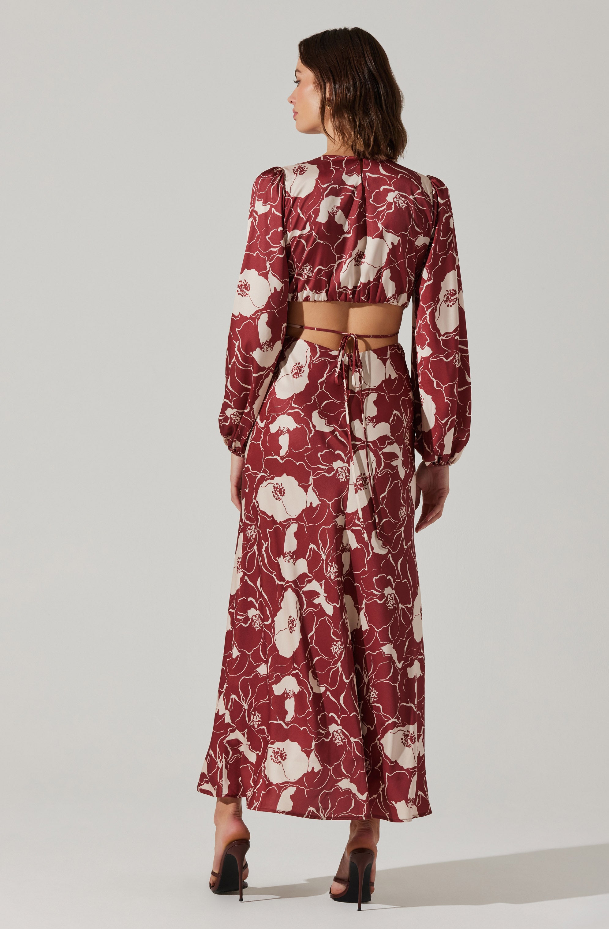 The outfit features a long, flowy skirt and a matching crop top with a floral pattern of large white flowers on a red background. The crop top has long, puffed sleeves and a gathered neckline, while the skirt is high-waisted with a tied waistband. The fabric appears lightweight and soft, creating an elegant and fashionable appearance.