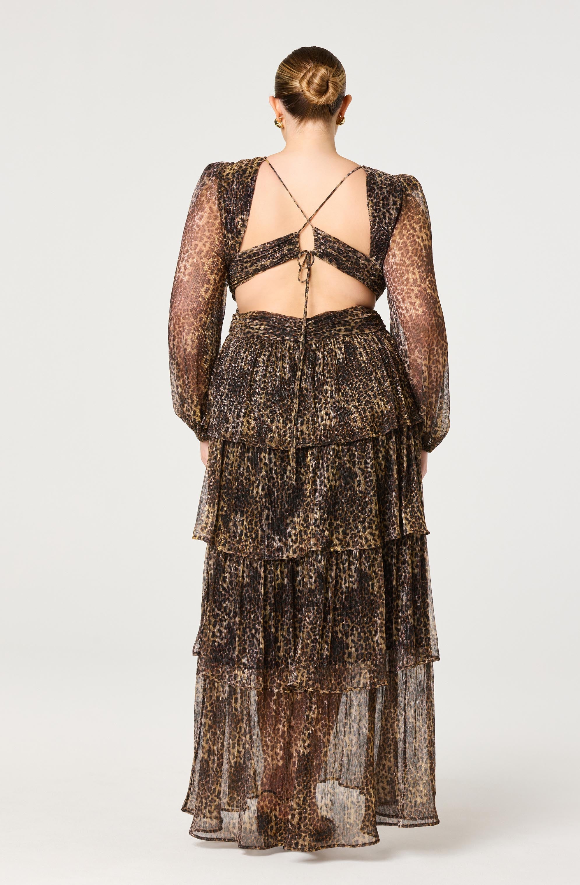A woman is wearing a sheer, long-sleeved dress with a leopard print pattern. The dress features a fitted bodice with puffed sleeves and a layered, tiered skirt that reaches the floor. The fabric is lightweight and semi-transparent.
