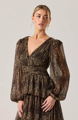 A woman is wearing a long-sleeved dress with a leopard print pattern. The dress features a deep V-neckline, puffed sleeves gathered at the wrists, a fitted waist with a matching fabric band, and a layered, ruffled skirt. The fabric appears lightweight and slightly sheer. She is accessorized with earrings and rings.