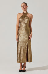 A woman is wearing a long, gold metallic gown with a halter neckline that features a twist front and a keyhole cutout at the bust. The dress has a high slit in the front, revealing her legs, and she is paired with black ankle-strap heels.