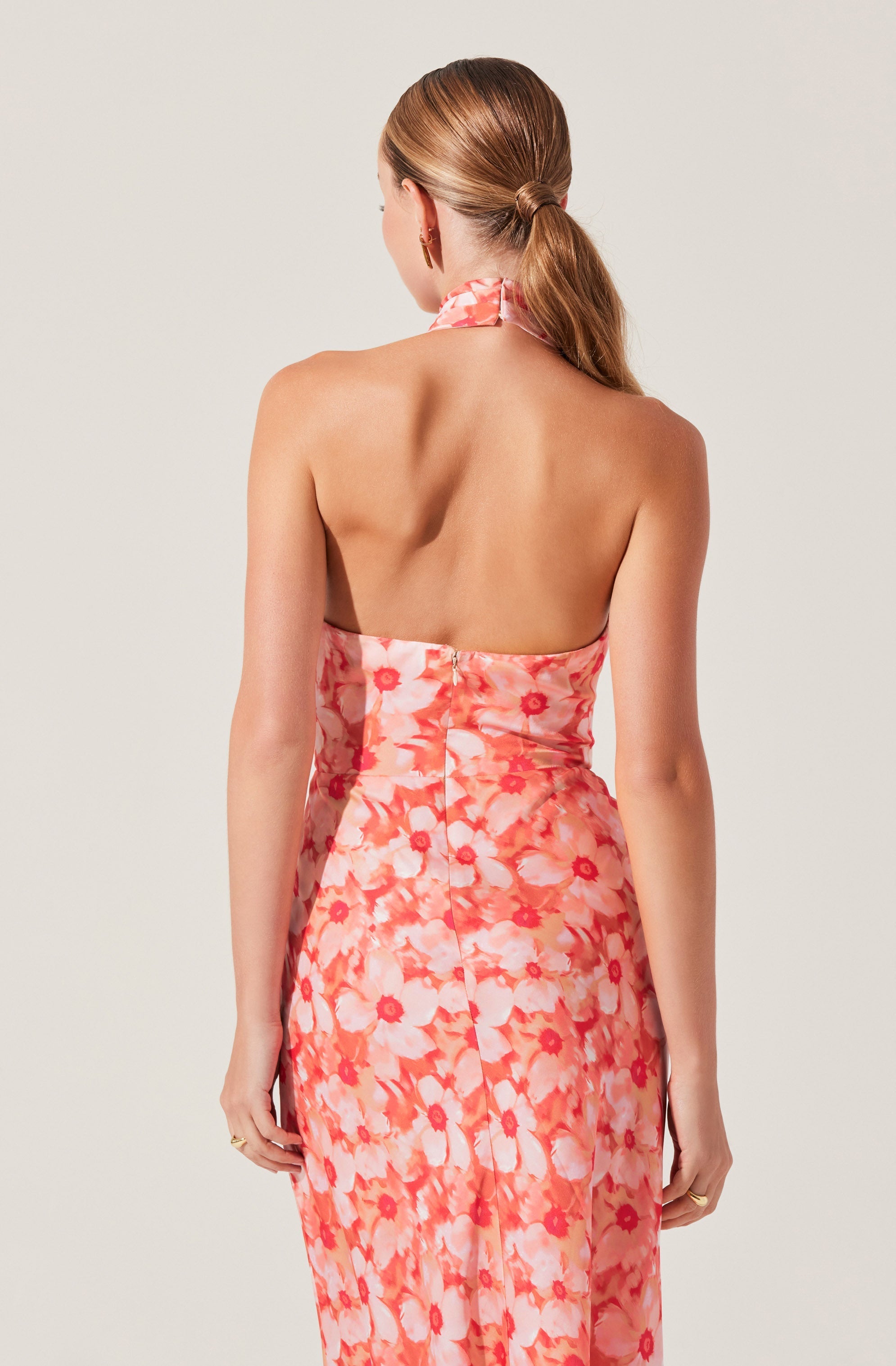 A woman is wearing a strapless dress with a floral pattern in shades of pink, coral, and white. The dress features a halter neckline with a matching fabric tie around the neck and has a fitted waist. The back of the dress is shown in the image.