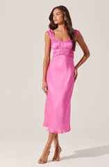 A woman is wearing a sleeveless, pink, satin maxi dress with ruched detailing on the bodice and ruffled shoulder straps. She accessorizes with gold earrings and strappy high-heeled sandals.