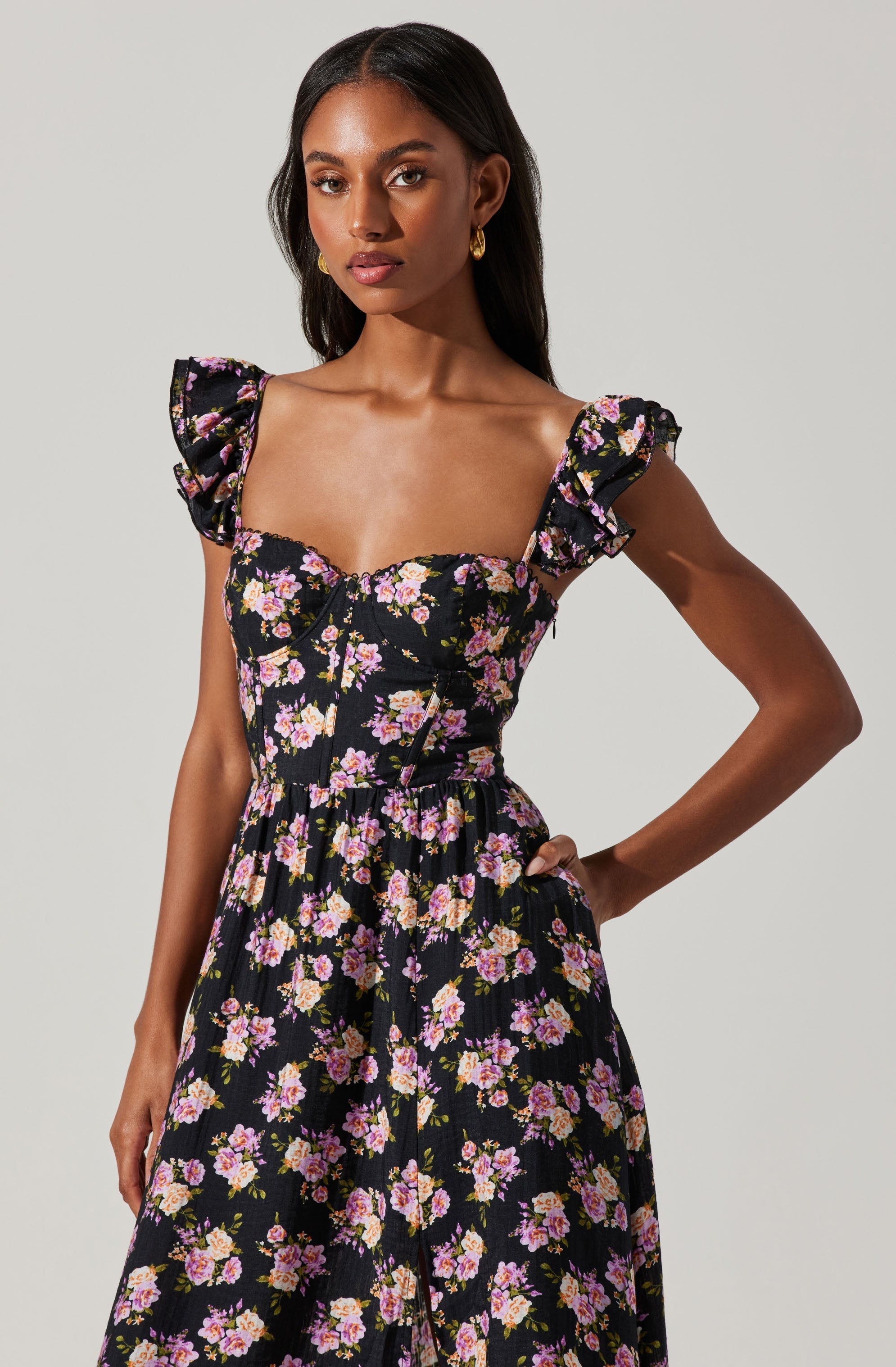 A woman wearing a black dress with a pink and purple floral pattern, featuring puffed short sleeves with ruffles and a fitted bodice with a zipper down the front.
