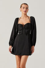 A woman is wearing a black dress with long, puffed sleeves made of shiny satin material. The top of the dress features a ruched bust with a small keyhole opening tied with a bow, and the dress has thin shoulder straps. The skirt is A-line and ends above the knees.