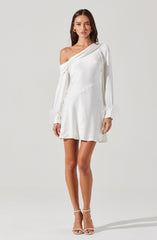 A woman is wearing an elegant white dress with an asymmetrical off-the-shoulder neckline on her left side. The dress has long sleeves with feathered cuffs and a slightly flared skirt that falls above the knees. The fabric appears smooth and shiny, giving it a sophisticated look. She is also wearing white high-heeled sandals.