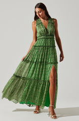 A woman is wearing a sleeveless, green, tiered maxi dress with a deep V neckline. The dress features a small slit on the right side, revealing her leg. The fabric has a floral pattern, and the dress has a gathered waistband. She is wearing beige high-heeled sandals.