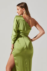 A woman is wearing a shiny, satin-like, bright green gown with an asymmetrical design. The gown has one long sleeve and exposes her left shoulder and arm, while the right side features a high slit revealing her leg. The dress fits snugly at the waist, accentuating her figure.