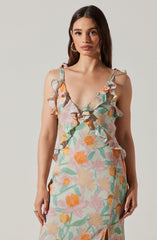 A woman is wearing a sleeveless dress with ruffled shoulder straps. The dress features a colorful, floral pattern with shades of orange, pink, green, and yellow. The fabric appears lightweight and semi-transparent, with a textured surface.