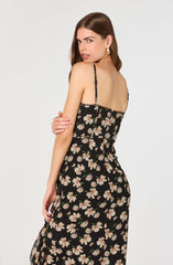 A woman is wearing a black dress with a floral pattern of white and pink flowers with green leaves. The dress has thin, adjustable spaghetti straps.