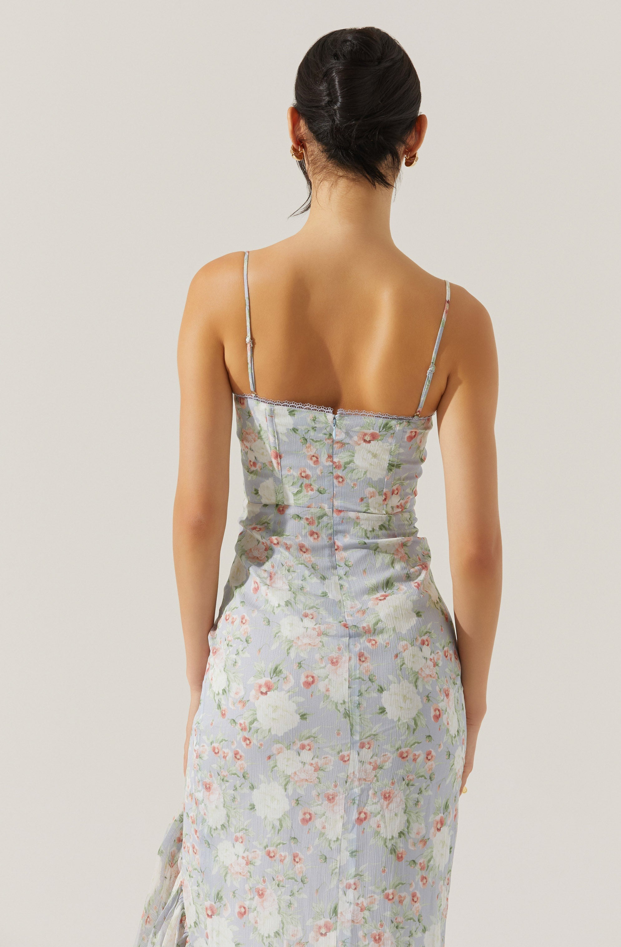 A person is wearing a sleeveless, floral-patterned dress with thin spaghetti straps. The dress features a fitted bodice and a long skirt with a soft, pastel-colored floral print.