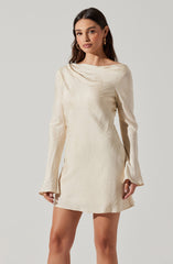 A woman is wearing a cream-colored, long-sleeved mini dress with a subtle shiny, textured pattern. The dress has a high, rounded neckline with a soft, draped collar detail. The sleeves are slightly flared at the cuffs.
