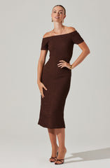 A woman is wearing an off-the-shoulder, knee-length dress in a textured, dark brown fabric. The dress features short sleeves and a fitted silhouette.