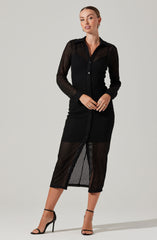 A woman is wearing a black, long-sleeved button-up dress made of a see-through, mesh fabric with a striped pattern. The dress has a collar and a front slit that reveals her legs. She is also wearing black high-heeled sandals with ankle straps.