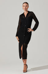 A woman is wearing a long, black, button-down dress made of a sheer, open-knit fabric. The dress features a collar, long sleeves, and a slit in the front that reveals her leg. She is also wearing black high-heeled sandals.