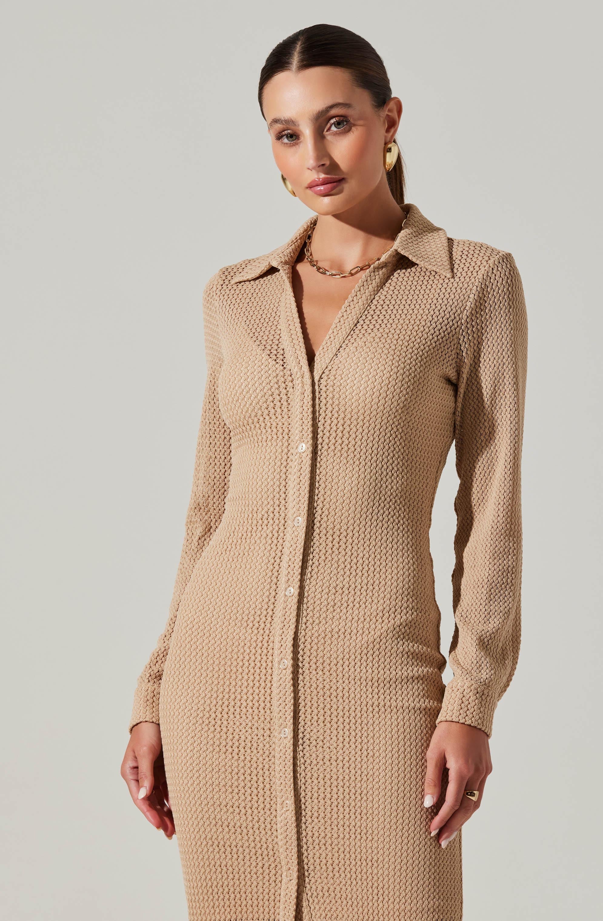 A woman is wearing a long, beige, textured dress with a collar and button-down front. The dress has long sleeves and a fitted silhouette. She is accessorized with gold hoop earrings, a gold chain necklace, and a ring on her right hand.