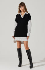A woman is wearing a white shirt with thin black vertical stripes beneath a black sleeveless knit sweater vest. The shirt extends below the vest, creating a layered look, and the hem of the shirt is slightly longer in the back. She is also wearing a short, matching striped skirt and knee-high black patent leather boots.