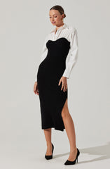 A woman is wearing a white button-up shirt with long sleeves underneath a black, strapless, ribbed knit dress that extends to mid-calf length with a side slit. She is also wearing black high-heeled shoes and gold hoop earrings.
