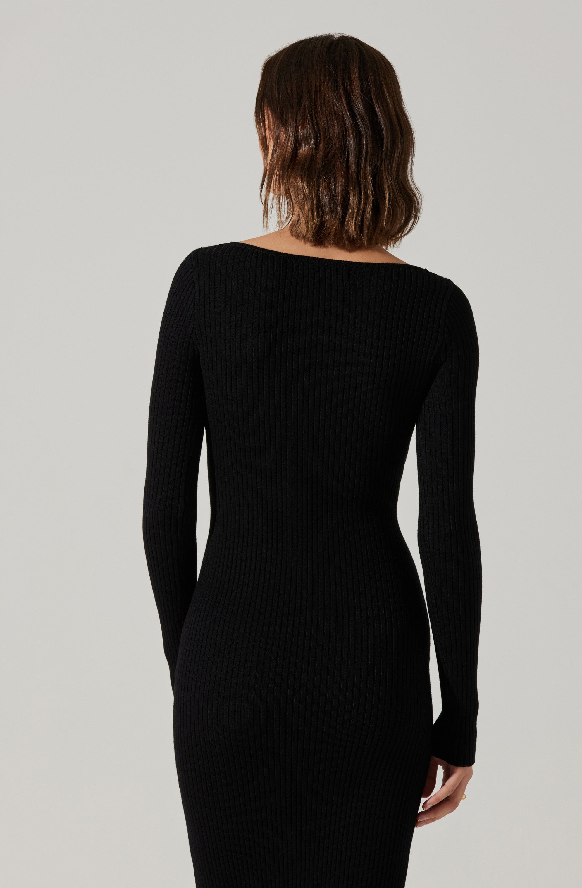 A woman is wearing a long, fitted black ribbed knit dress with long sleeves. The dress has a simple, elegant design, and the fabric features vertical ribbing throughout.