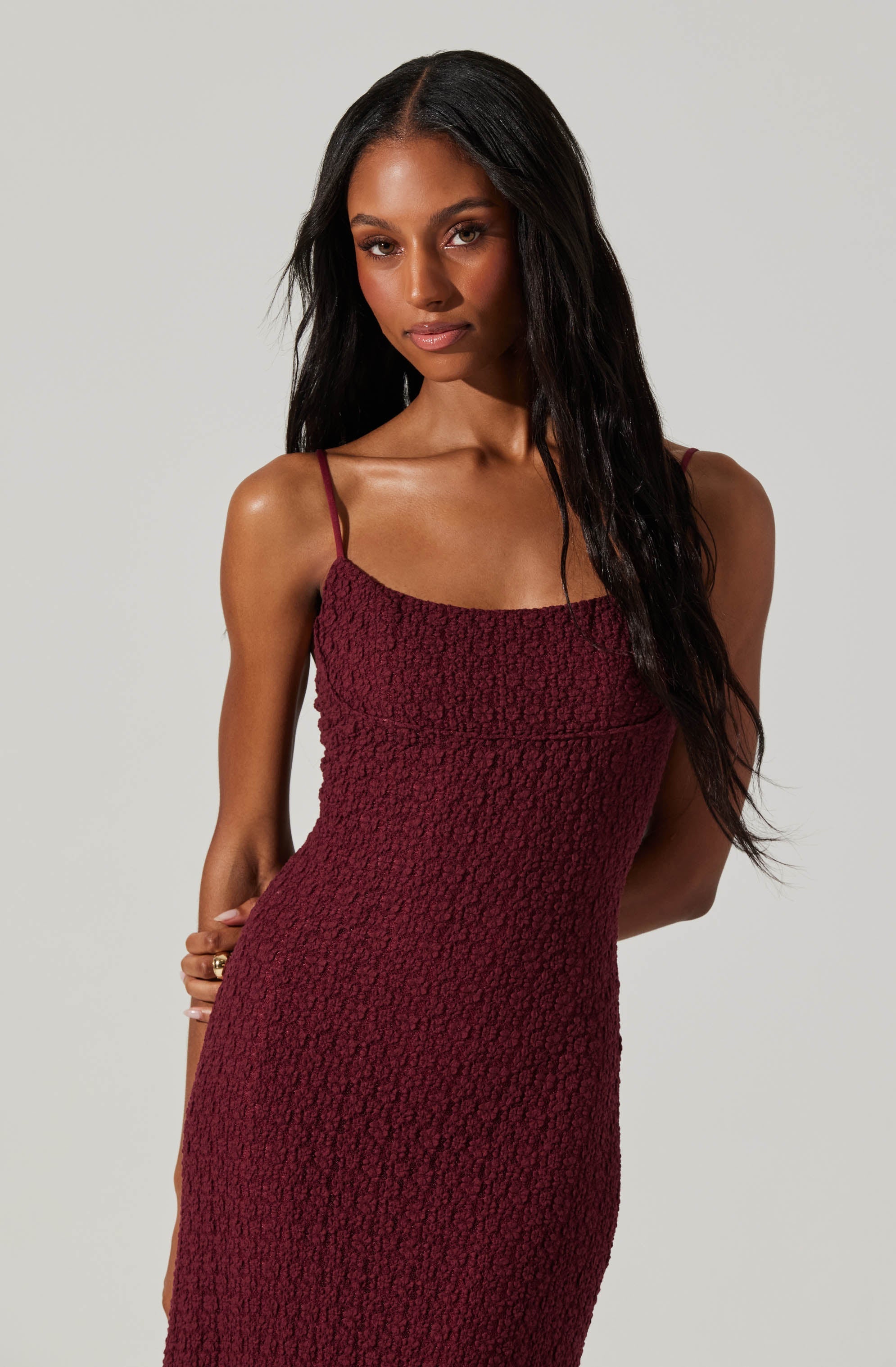 A woman wearing a fitted, textured, deep red dress with spaghetti straps.
